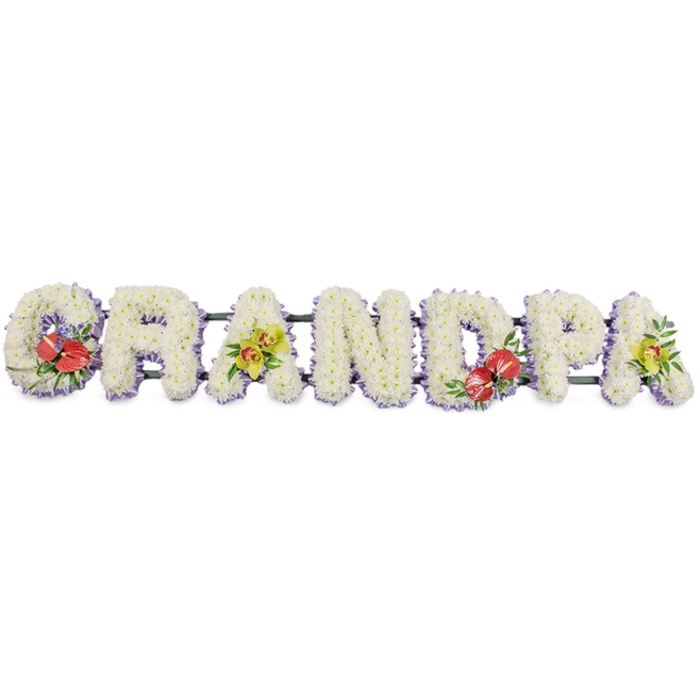A dignified floral name tribute stretches horizontally to spell "GRANDPA," each letter standing strong and clear against a simple white background, as if ready to be placed beside a coffin or at a memorial service in Wennington. The letters are crafted from masses of small, snowy white chrysanthemums, set so tightly together that no gaps show, creating a smooth yet textured surface that looks like a soft, floral carpet. Their pure white colour conveys serenity and farewell, while a slim band of light lavender ribbon runs around the base of each letter, forming a subtle border that lifts the design with a gentle wash of pastel purple. This lilac trim adds depth and definition when viewed from the side, helping each letter stand out while still keeping the overall look harmonious and understated. The letters are fixed to dark green bars, which provide hidden strength, suggesting a tribute made to travel safely from a local Wennington home to the crematorium or church. Rich accent sprays bring colour and personality: the 'G' and the 'D' feature eye-catching groupings of deep red anthuriums, their glossy, heart-shaped spathes and prominent central spadices surrounded by lush green foliage and perhaps touches of small purple filler blooms. These bold, passionate reds convey love and devotion. In contrast, the first and last 'A' are adorned with clusters of yellow-green orchids, their delicate petals and exotic centres arranged with graceful leaves, adding an air of refined elegance and enduring beauty. The overall design feels calm, balanced, and thoughtfully composed-a bespoke memorial that quietly honours a beloved grandfather, capturing the tenderness and respect his family feel as they say goodbye.
